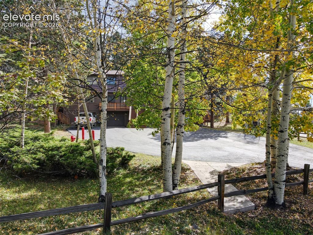 Image 47 of 50: Split-rail fence framing the property, mature deciduous trees, evergreen sh