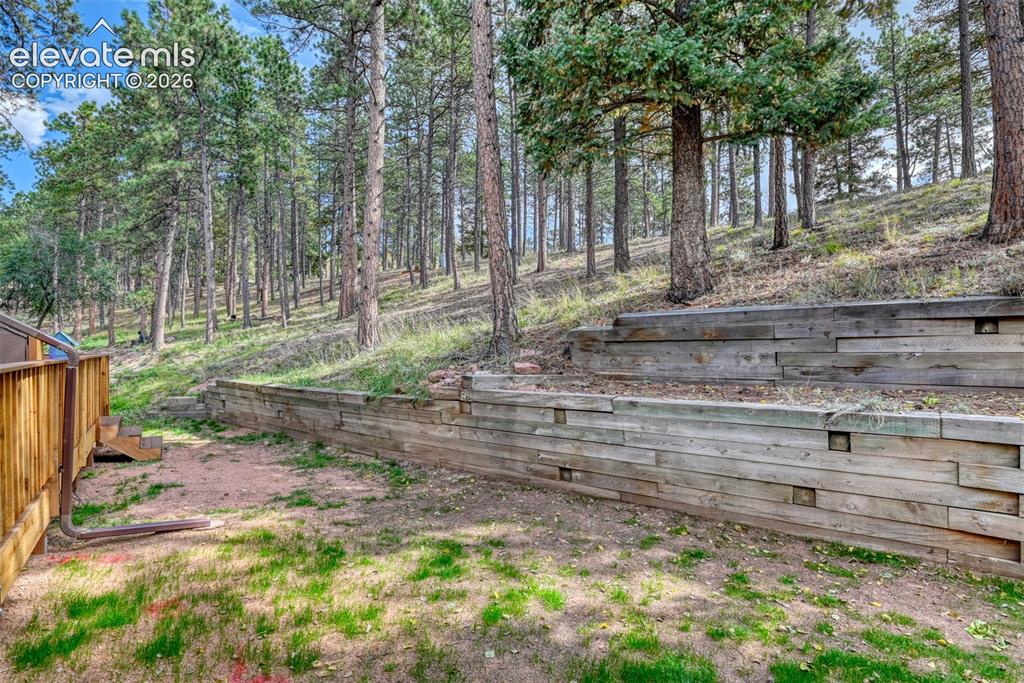 Image 5 of 50: Wood retaining walls, terraced landscaping, and a natural tree-lined backdr