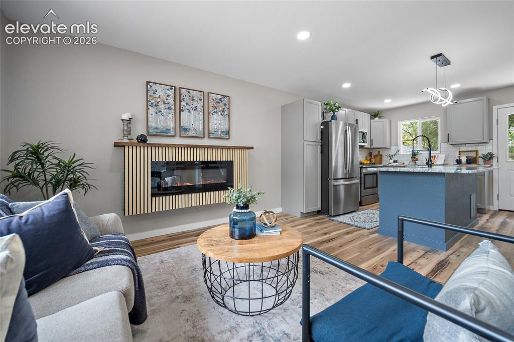 Image 14 of 49: Open-concept living space with wood-finish flooring, a wall-mounted electri