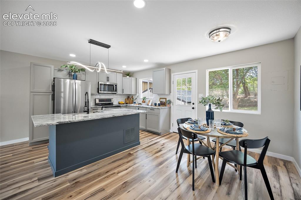 Image 15 of 49: Kitchen featuring light wood-finish flooring, a dark blue island with a lig