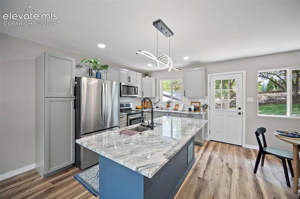 Image 20 of 49: Kitchen featuring a central island with a stone countertop, light grey cabi