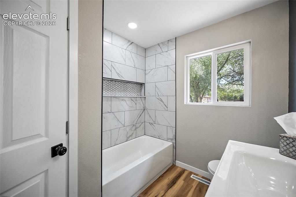 Image 24 of 49: Contemporary bathroom featuring a white tub, patterned tile surround with a