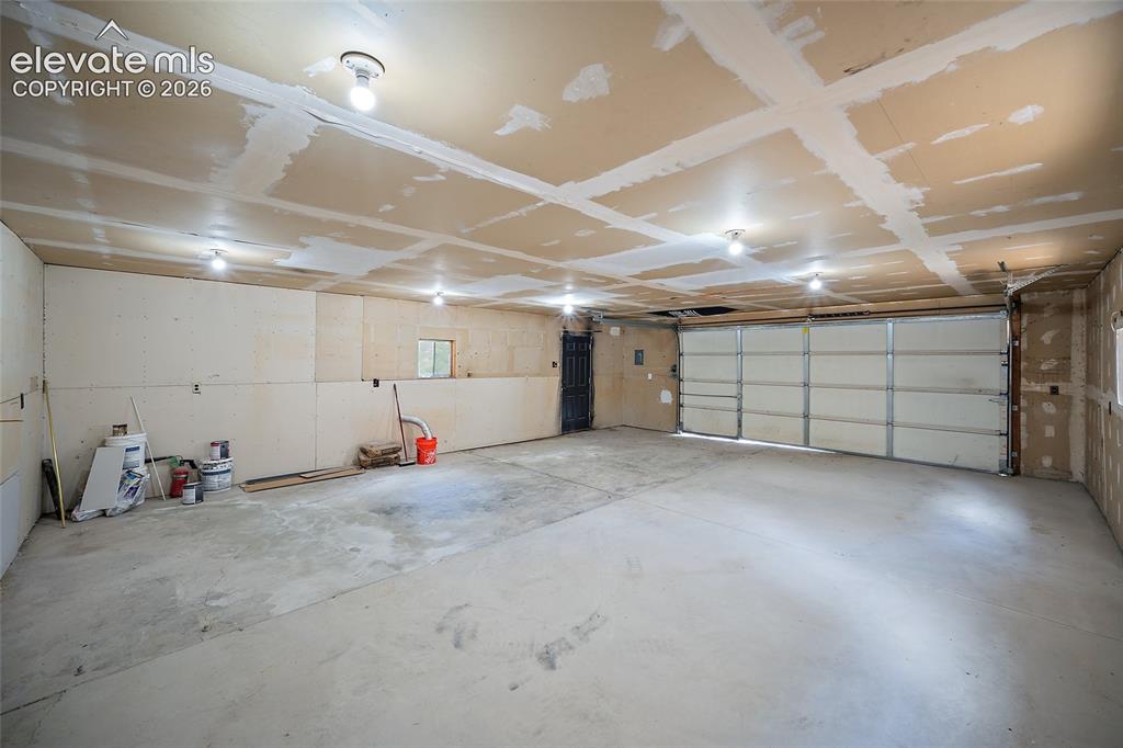 Image 38 of 49: Spacious garage with exposed framing, concrete flooring, and multiple ceili