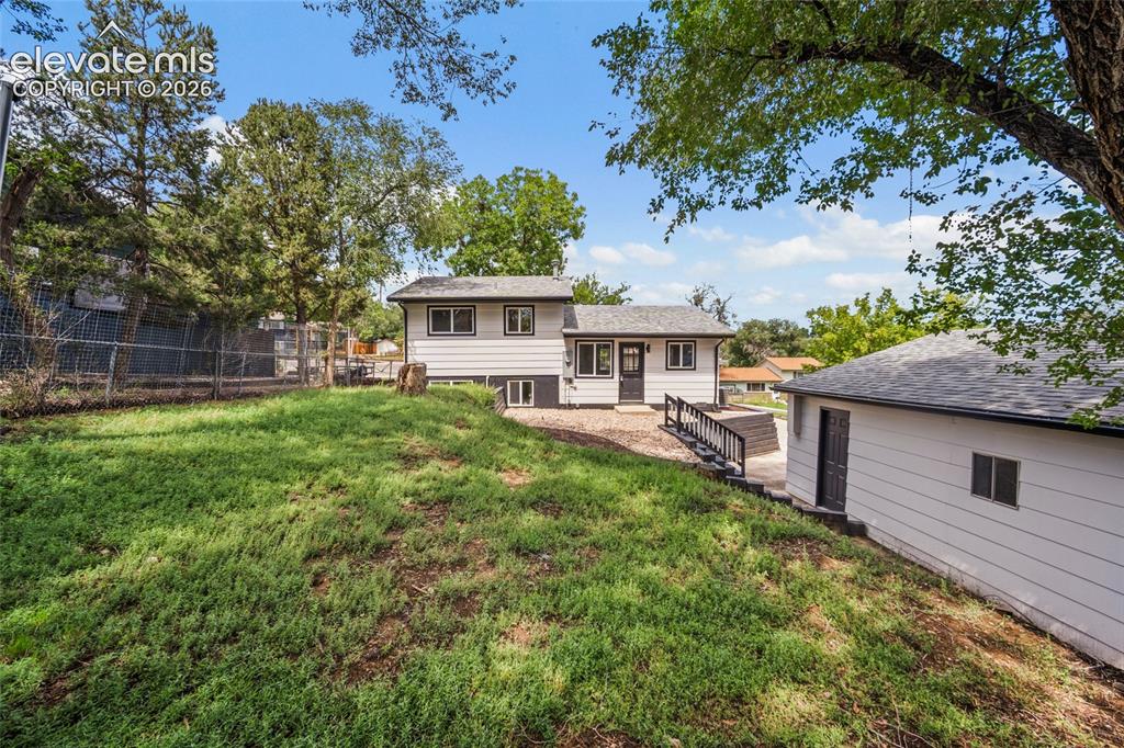 Image 39 of 49: Expansive sloped lawn with mature trees, featuring a detached garage with a