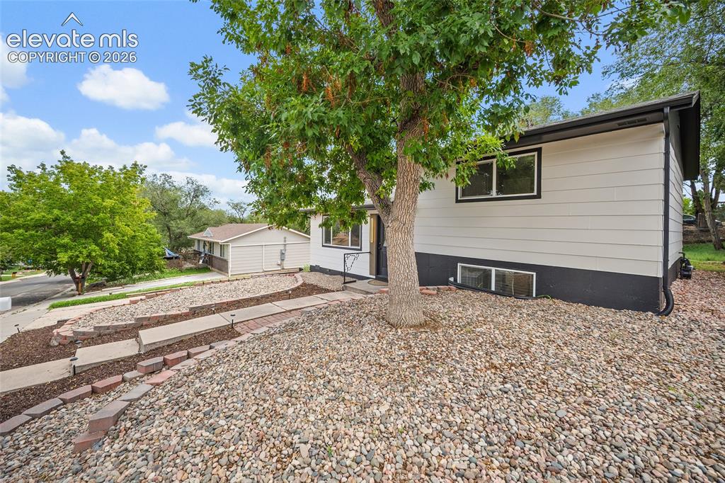 Image 5 of 49: Exterior featuring light-colored siding, dark trim, and a prominent mature