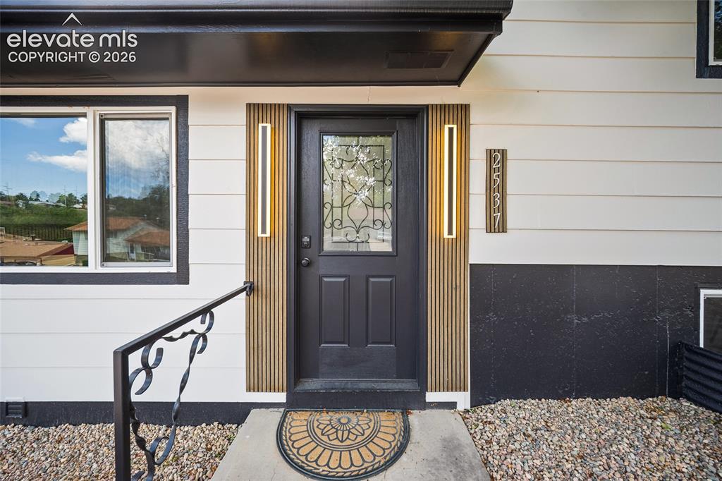 Image 7 of 49: Black paneled entry door with decorative glass inlay, flanked by vertical w
