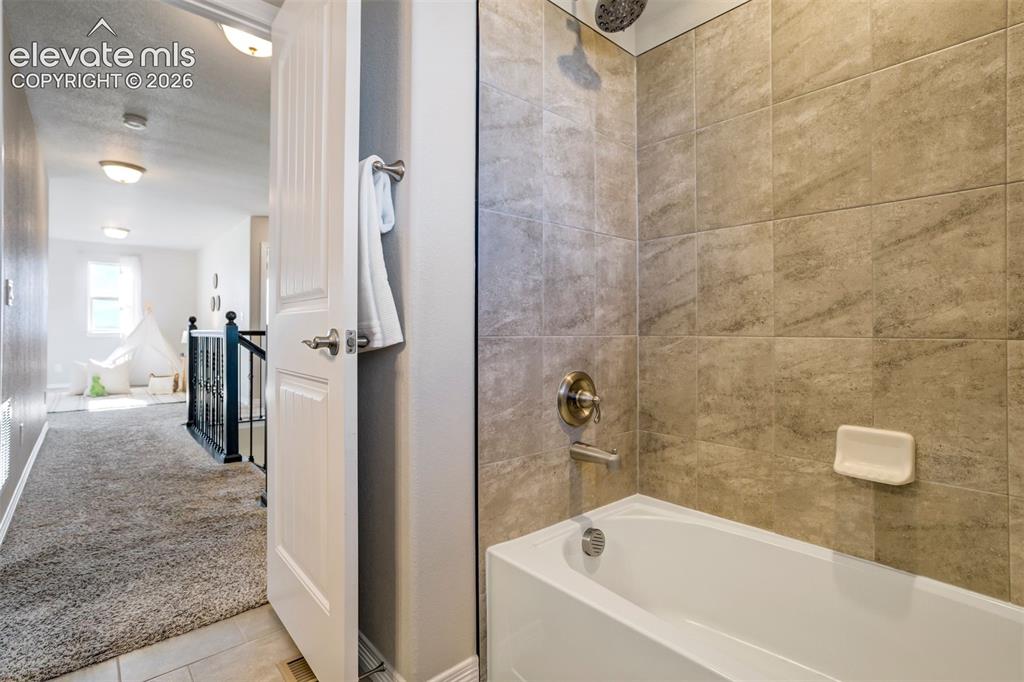 Image 31 of 47: Bathtub with tiled surround, brushed nickel fixtures, and a rain shower hea
