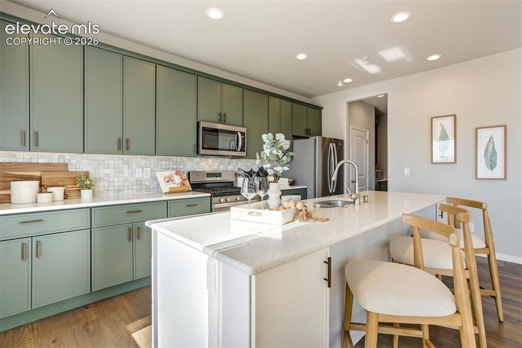 Image 7 of 47: Kitchen featuring green cabinetry, stainless steel appliances, a white tile