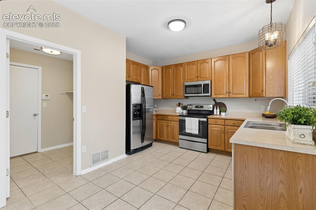 Image 12 of 26: Kitchen featuring wood cabinetry, stainless steel appliances, tile flooring
