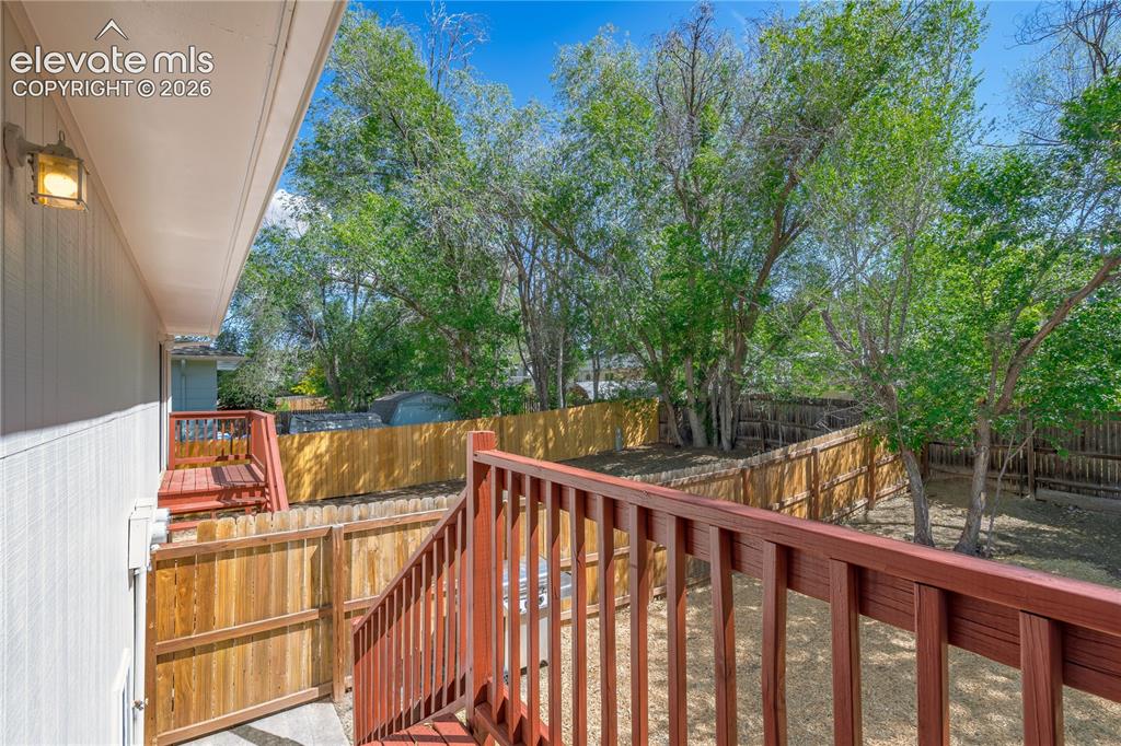 Image 28 of 32: Multi-level wood deck with stained railings, featuring a fenced backyard wi