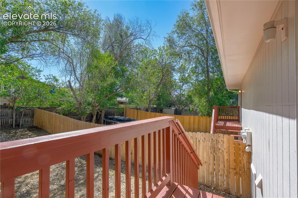 Image 8 of 32: Rear exterior featuring a red-stained wood deck with railings, a wood priva