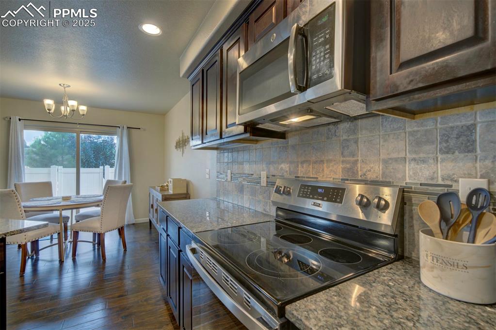 Image 11 of 34: Kitchen with stainless steel appliances, decorative backsplash, dark wood f