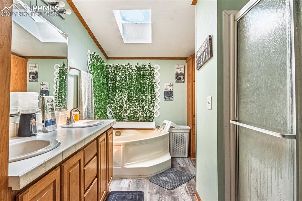 Image 20 of 48: Bathroom with a skylight, wood finished floors, a bath, double vanity, and 