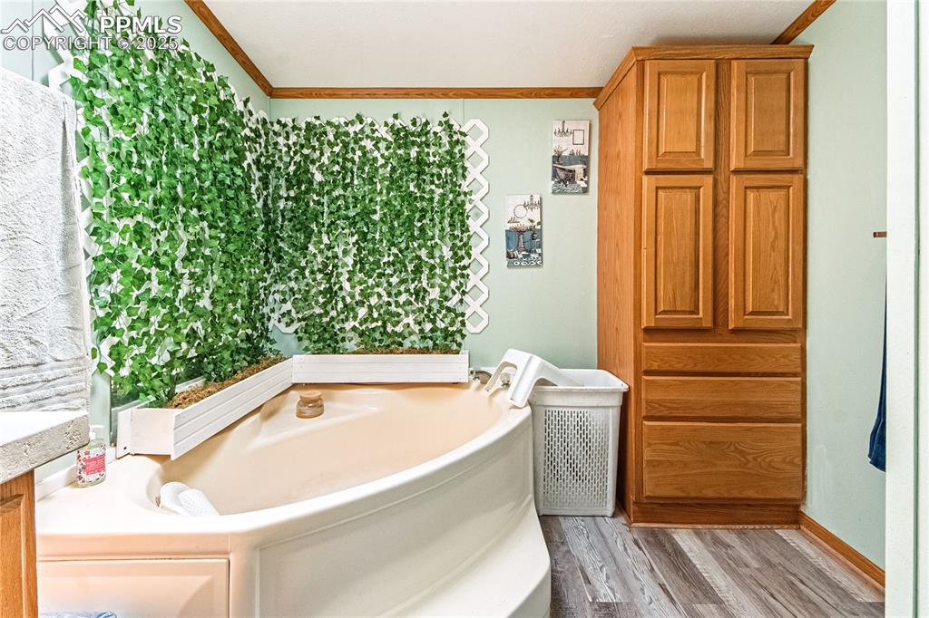 Image 22 of 48: Bathroom featuring a bath, wood finished floors, and ornamental molding