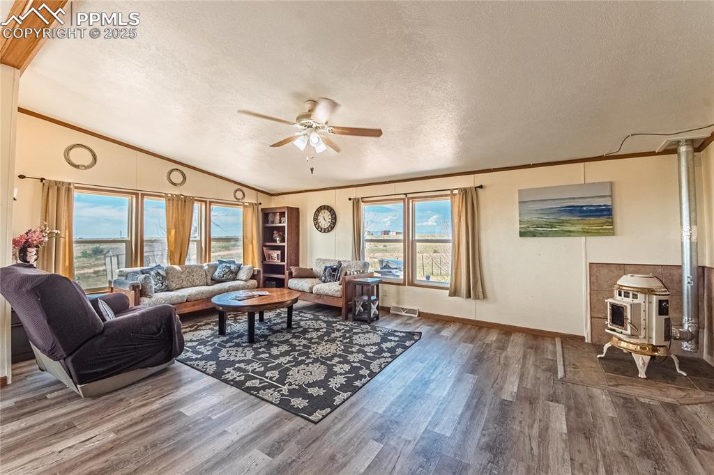 Image 9 of 48: Living area with a wood stove, a ceiling fan, lofted ceiling, a textured ce