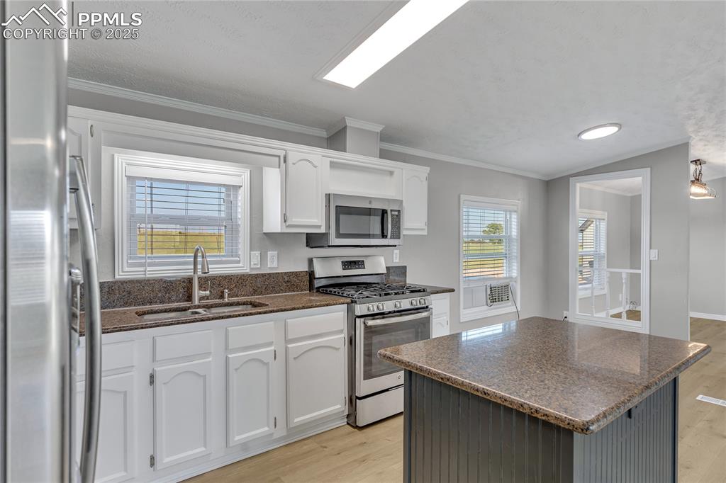 Image 13 of 34: Kitchen featuring white cabinets, lofted ceiling, sink, and appliances with