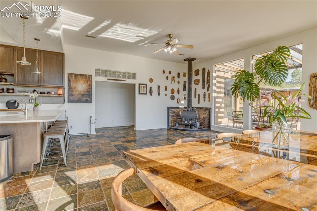 Image 10 of 47: Dining area with sink, dark tile floors, ceiling fan, and a wood stove
