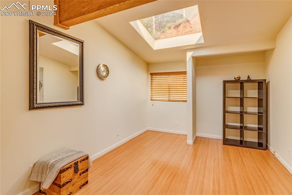 Image 27 of 47: Empty room with lofted ceiling with skylight and light wood-type flooring