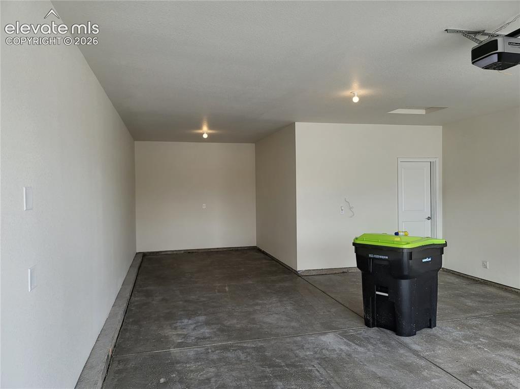 Image 25 of 25: Spacious garage featuring concrete flooring, white painted walls, and overh