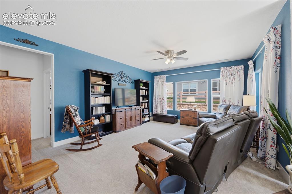 Image 7 of 25: Spacious living area featuring light-colored carpeting, multiple windows, a