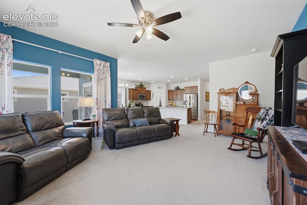 Image 8 of 25: Open-concept living area featuring light carpeting and a ceiling fan with i