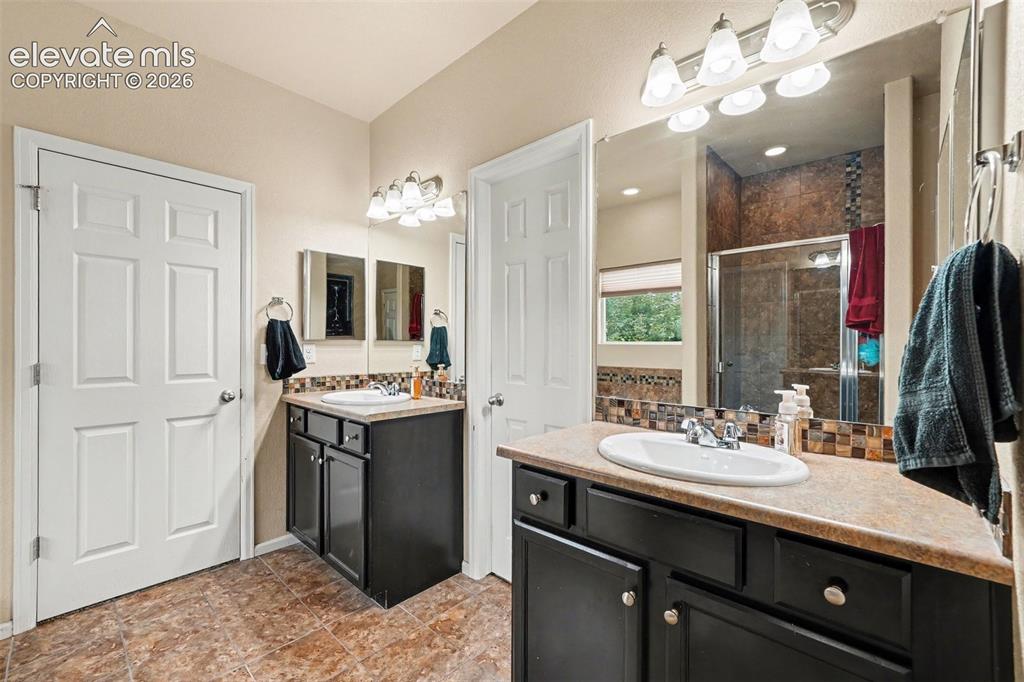 Image 8 of 21: Primary bath with dual vanity sinks, dark wood-finish cabinetry, a full-wid