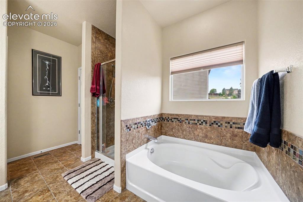 Image 9 of 21: Corner soaking tub, tiled shower enclosure, large window, and tiled floorin