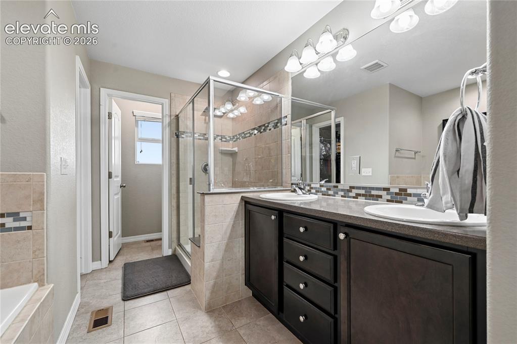 Image 29 of 48: The en-suite 5-piece master bathroom is wrapped in decorate ceramic tile wi