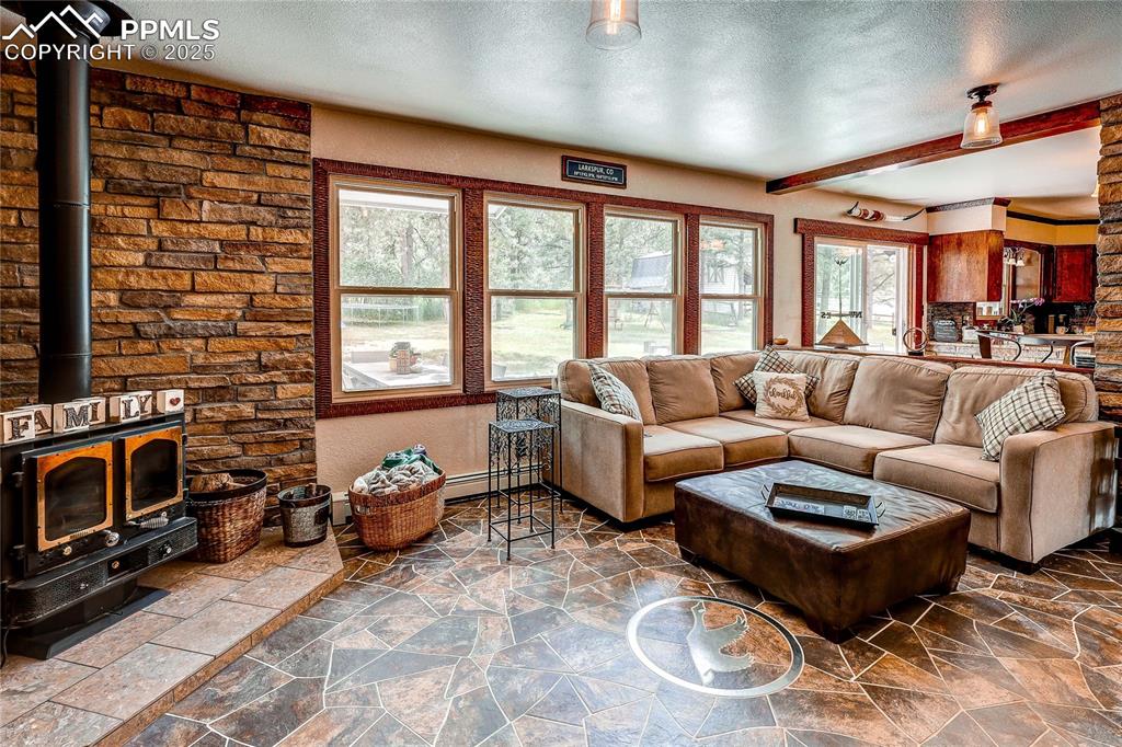Image 10 of 49: Living room featuring a textured ceiling, a wood stove, stone finish floors