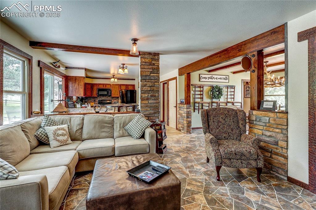 Image 11 of 49: Living room with beam ceiling, stone floors, and a textured ceiling