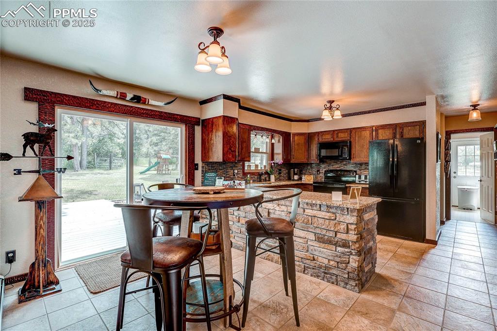 Image 12 of 49: Kitchen featuring black appliances, brown cabinetry, and backsplash