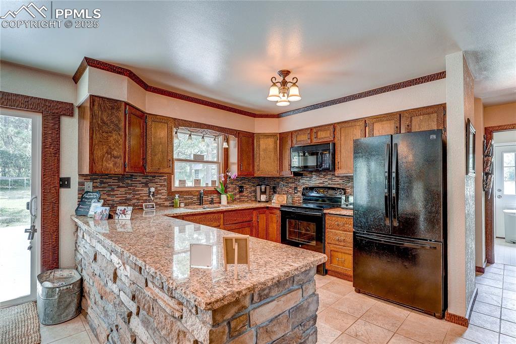 Image 13 of 49: Kitchen featuring black appliances, a peninsula, brown cabinetry, backsplas
