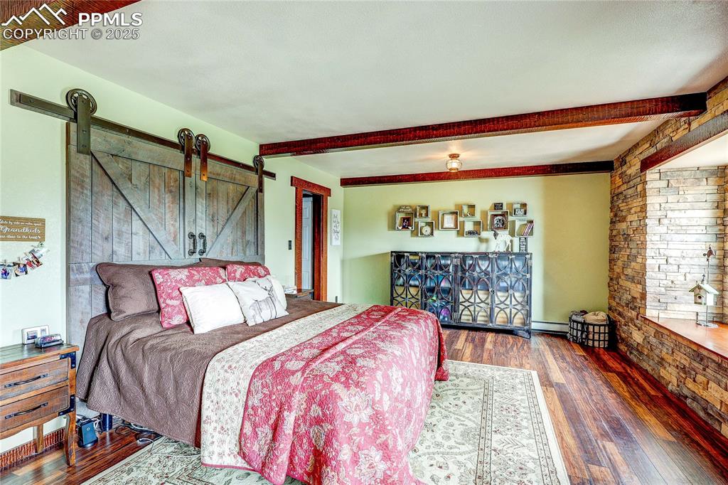 Image 21 of 49: Bedroom with hardwood / wood-style floors, beam ceiling, and a barn door
