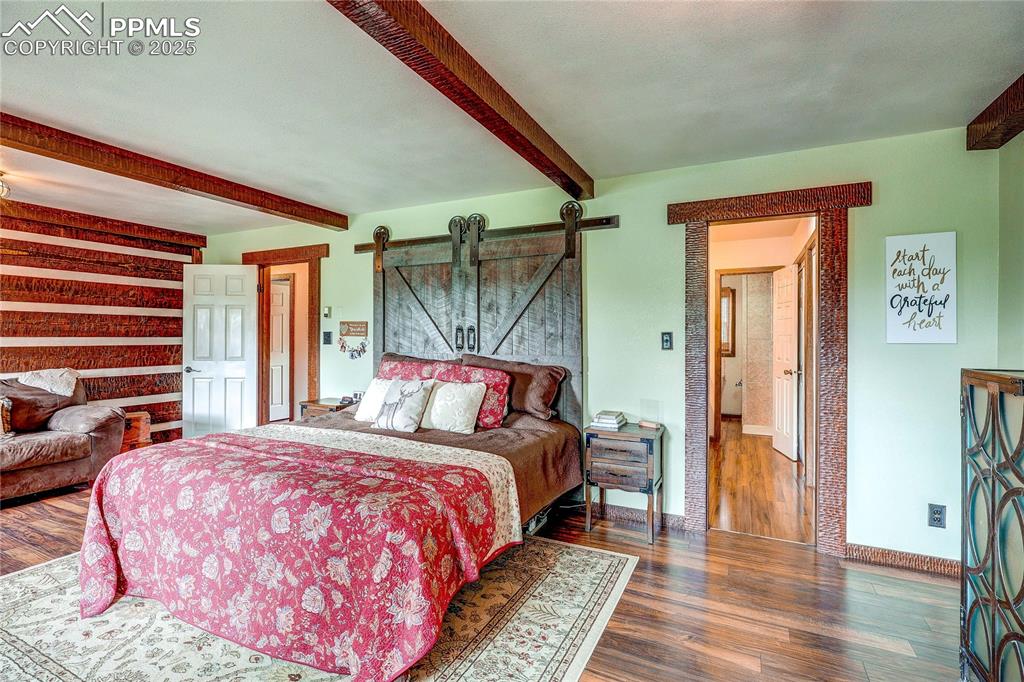Image 23 of 49: Bedroom featuring beam ceiling, a barn door, and wood finished floors