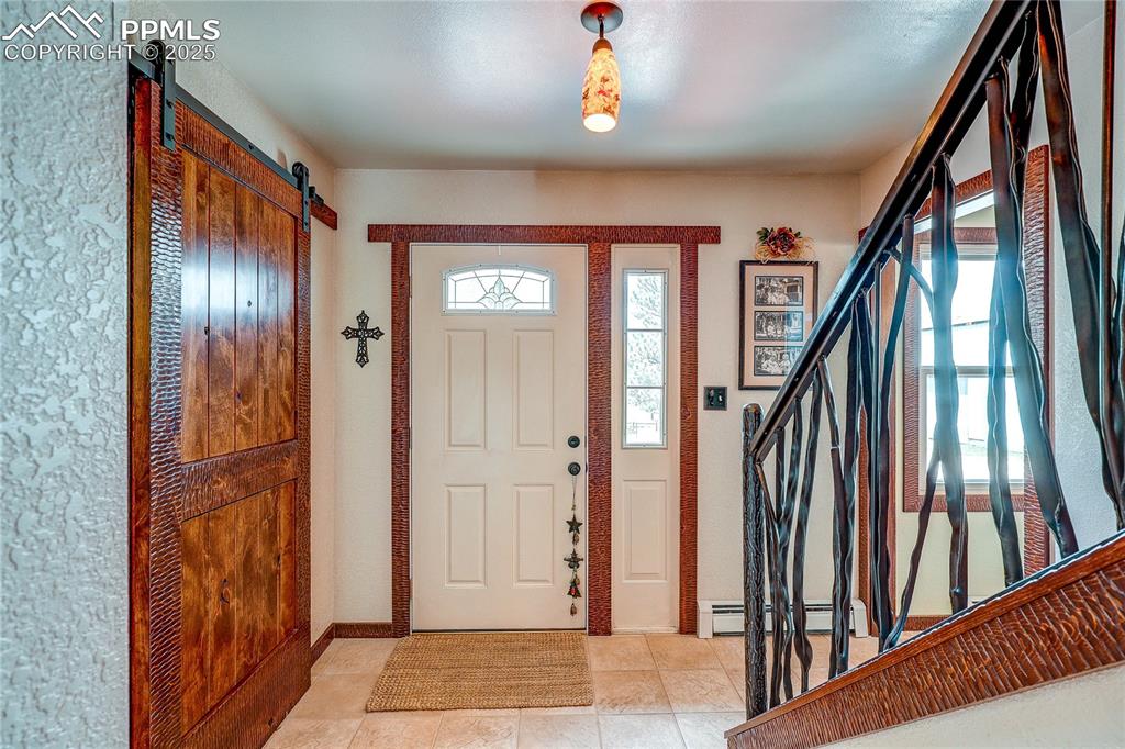 Image 3 of 49: Entrance foyer with a barn door, stairs, light tile patterned floors, and a
