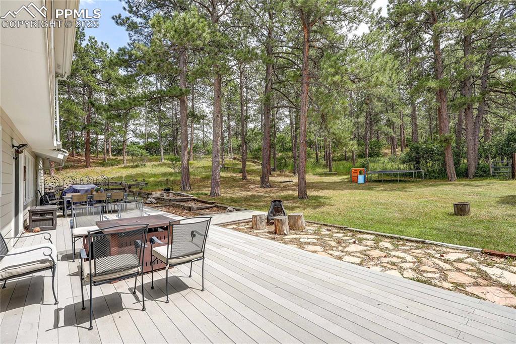 Image 36 of 49: Wooden terrace featuring outdoor dining space, a lawn, view of scattered tr