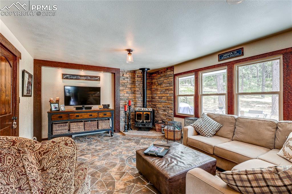 Image 9 of 49: Living area featuring stone finish flooring, a wood stove, and a textured c