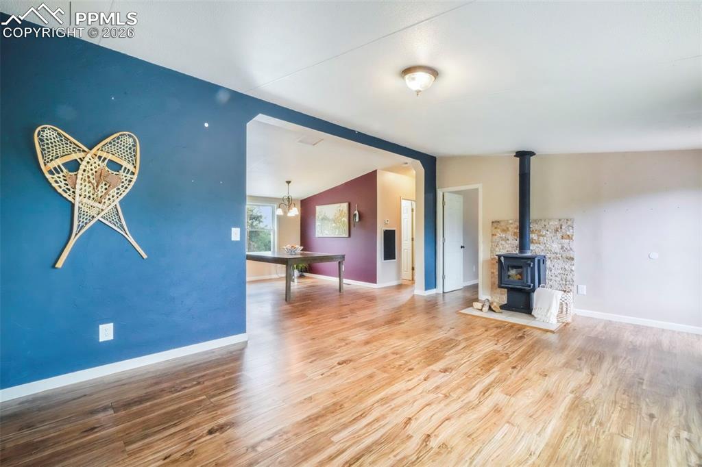 Image 14 of 50: Unfurnished living room with a wood stove, wood finished floors, lofted cei
