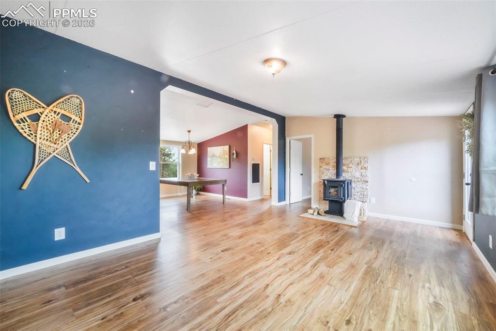 Image 15 of 50: Unfurnished living room with a wood stove, wood finished floors, lofted cei