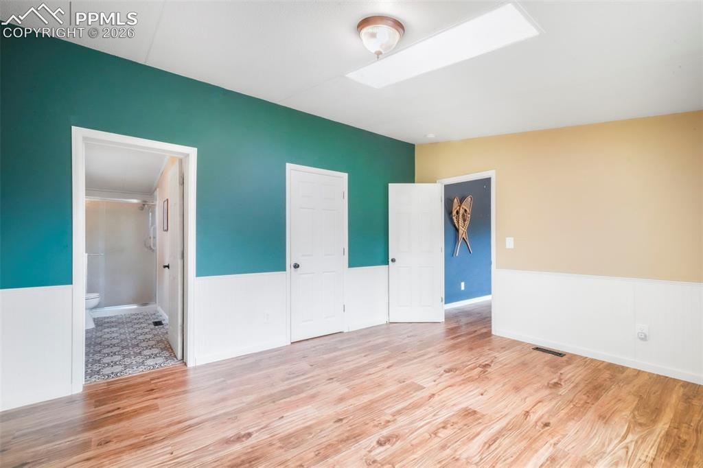 Image 26 of 50: Empty room with a wood stove, light wood-type flooring, wainscoting, and a