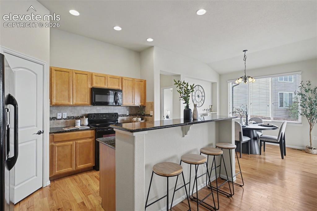 Image 10 of 39: Kitchen featuring light wood cabinetry, black appliances, dark countertops,