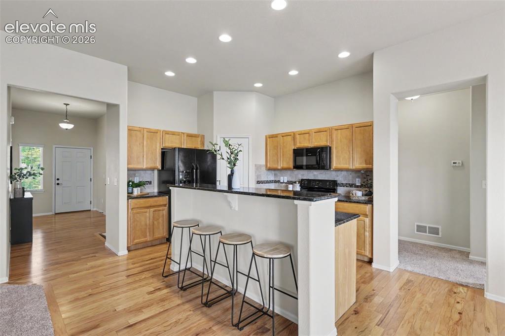 Image 11 of 39: Kitchen featuring light wood cabinetry, dark countertops, and a mosaic tile