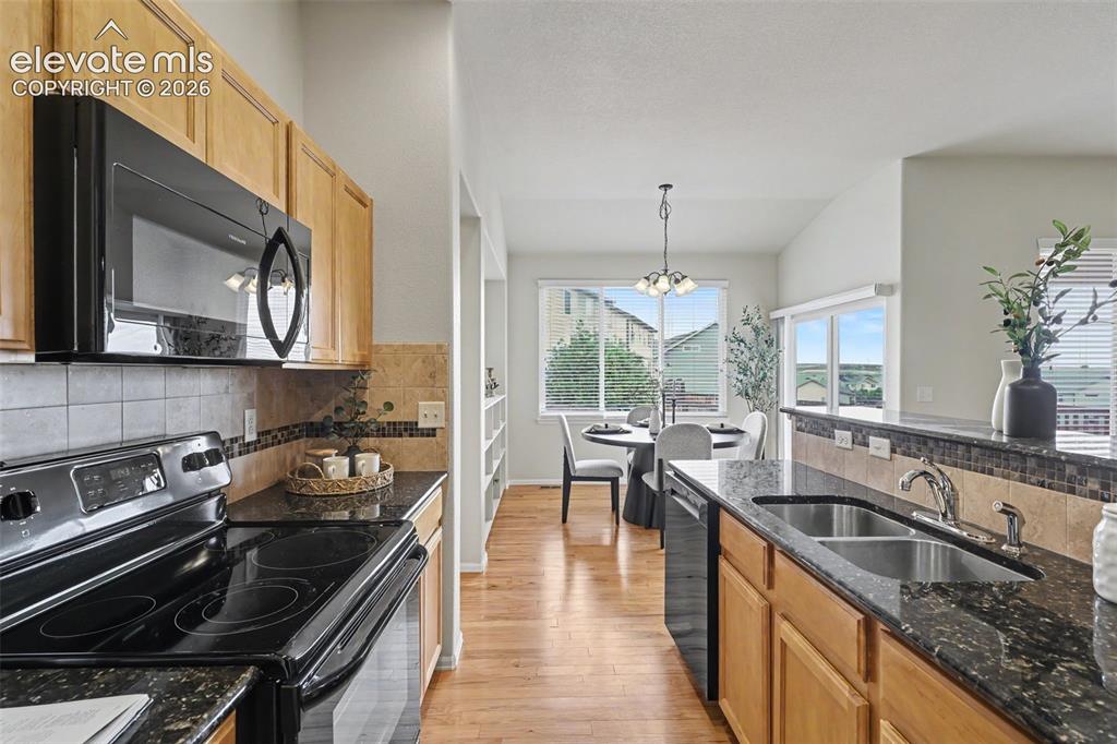 Image 14 of 39: Kitchen featuring wood-finish flooring, dark granite countertops, light woo