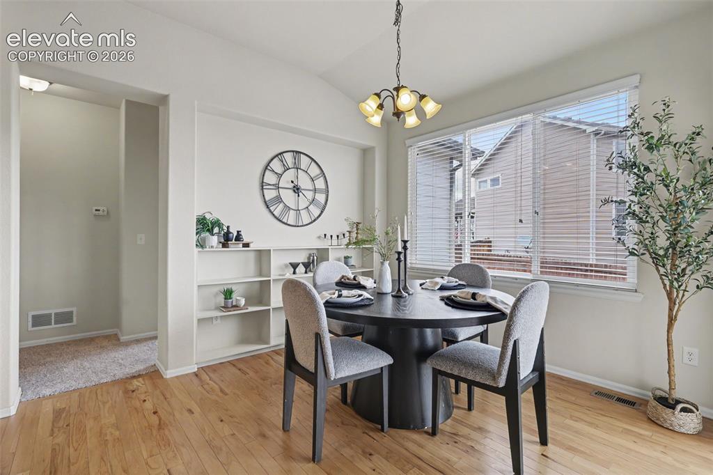 Image 16 of 39: Dining area featuring hardwood flooring, built-in shelving, vaulted ceiling