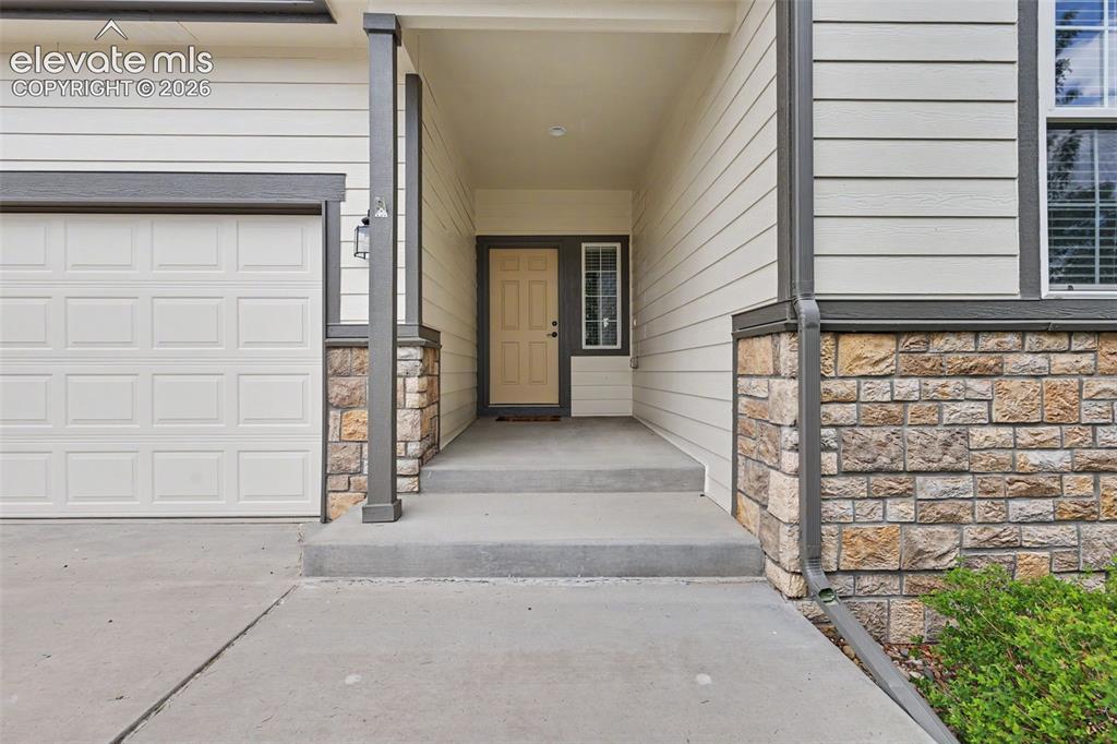 Image 3 of 39: Inviting entryway featuring a covered porch, stone veneer accents, concrete
