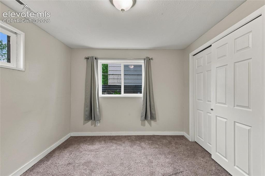 Image 26 of 34: Basement bedroom with carpet flooring, white trim, and two windows provide 