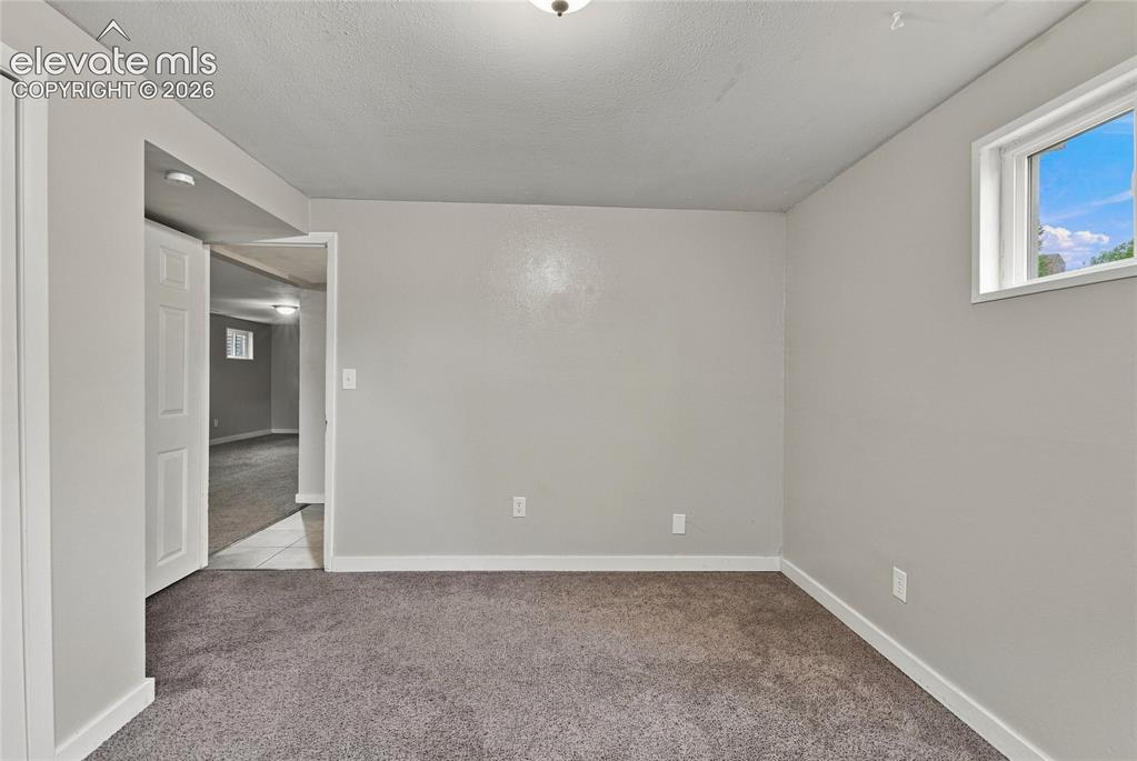Image 27 of 34: Basement bedroom with carpet flooring, white trim, and two windows provide 