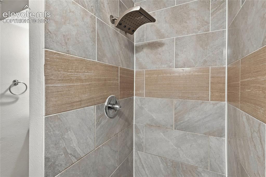 Image 29 of 34: Basement shower featuring large format light gray tiles with a wood-finish 