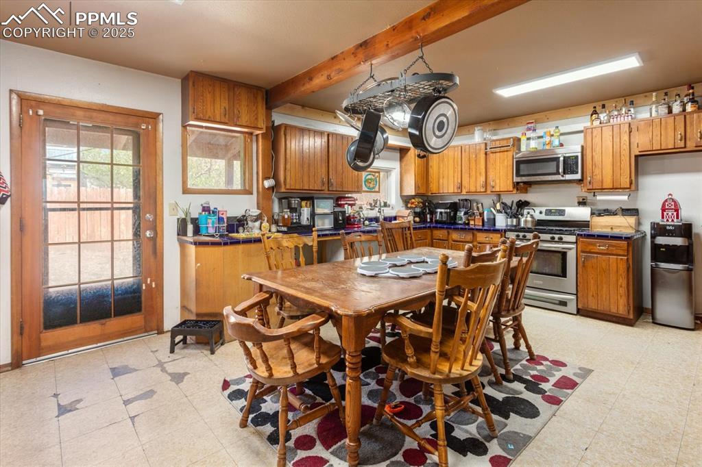 Image 11 of 45: Kitchen with stainless steel appliances, brown cabinetry, light floors, and