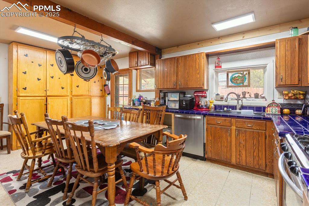 Image 13 of 45: Kitchen with stainless steel appliances, tile counters, a sink, light floor